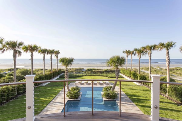 Beachfront property with swimming pool, manicured lawn, palm trees, and ocean view beyond dunes