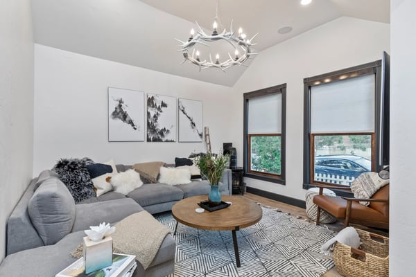 Modern living room with gray sectional sofa, round wood coffee table, antler chandelier, and large windows overlooking pool and grounds